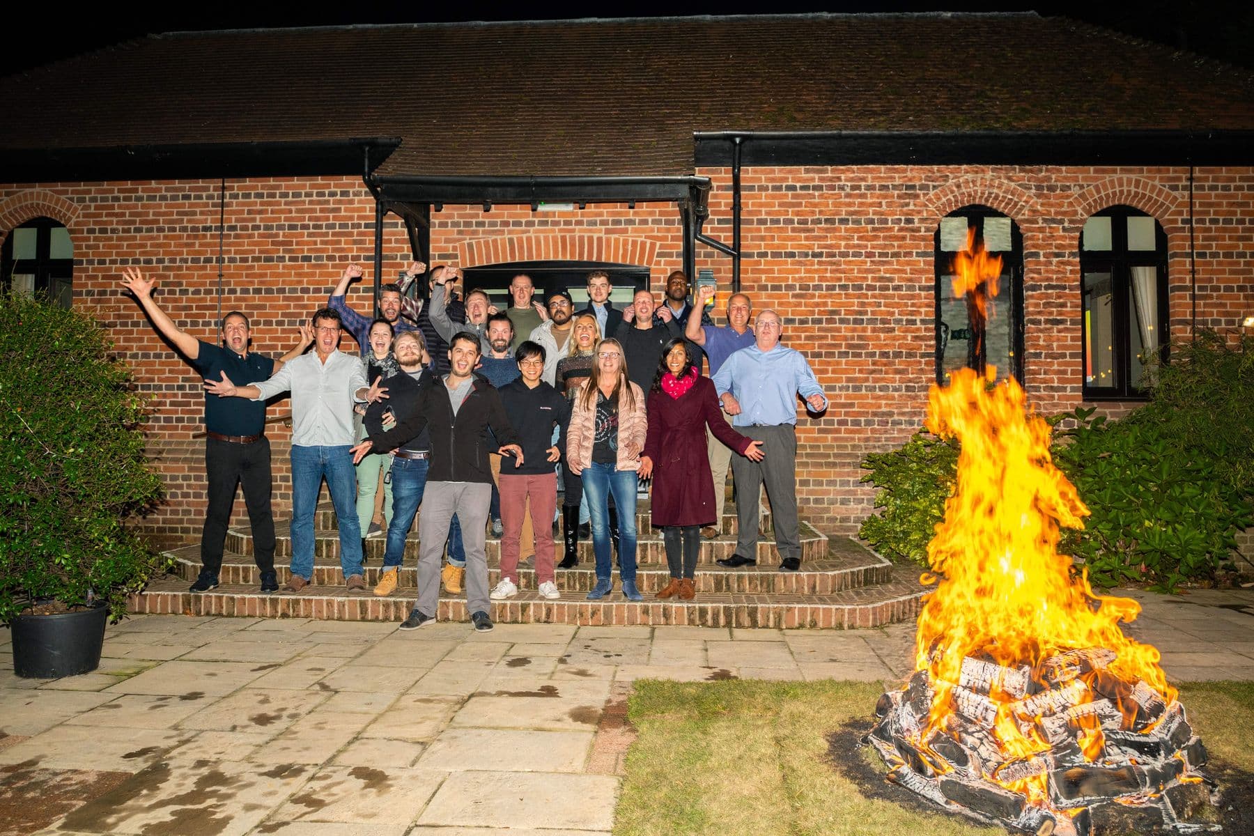 A group cheering in front of a building at night beside a blazing fire, before a fire walk