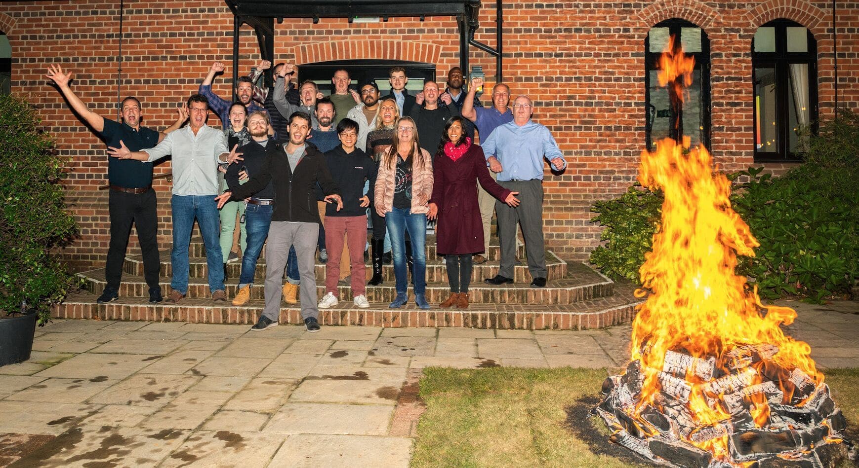 A group celebrating in front of a building at night beside a blazing fire before a fire walk