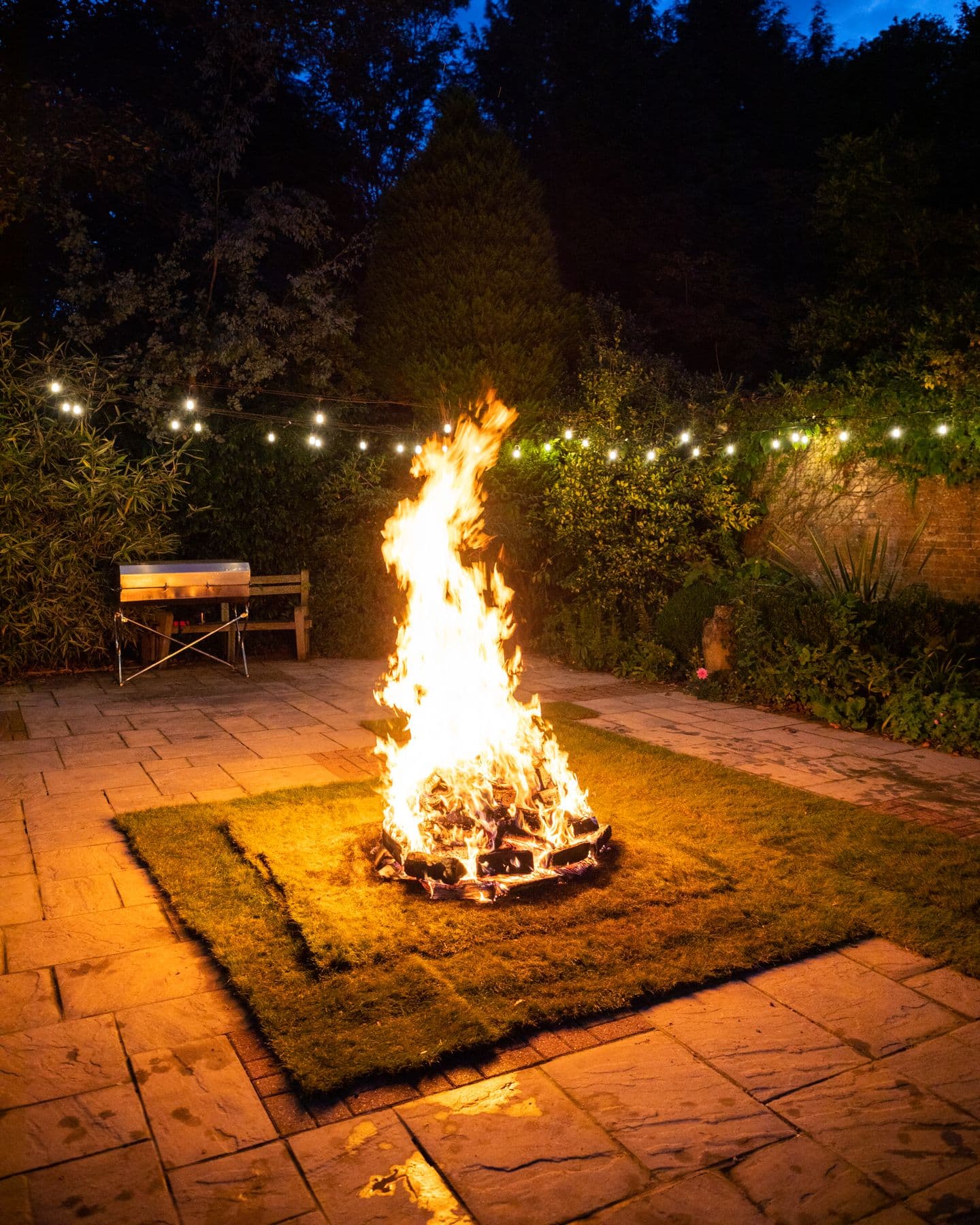 The fire for a fire walk burning on a lawn at night under festoon lights
