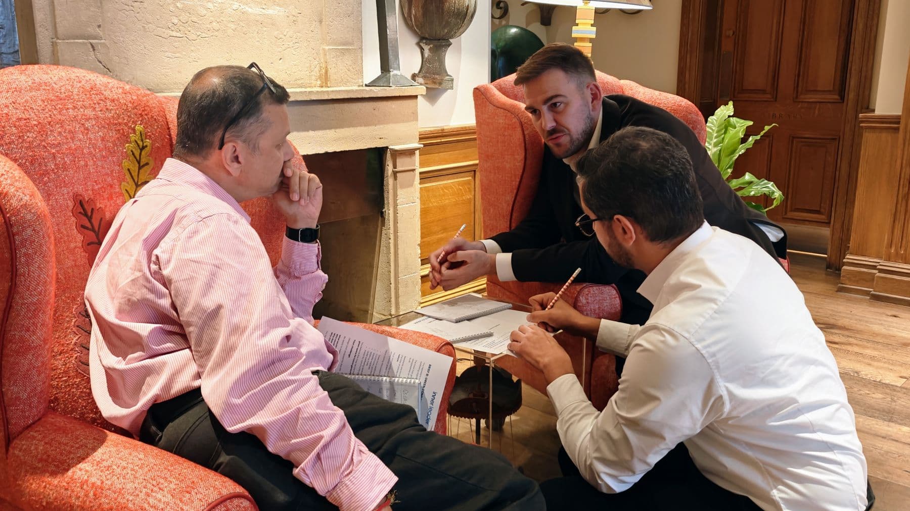 Three people working through a sales exercise together in armchairs by a fireplace
