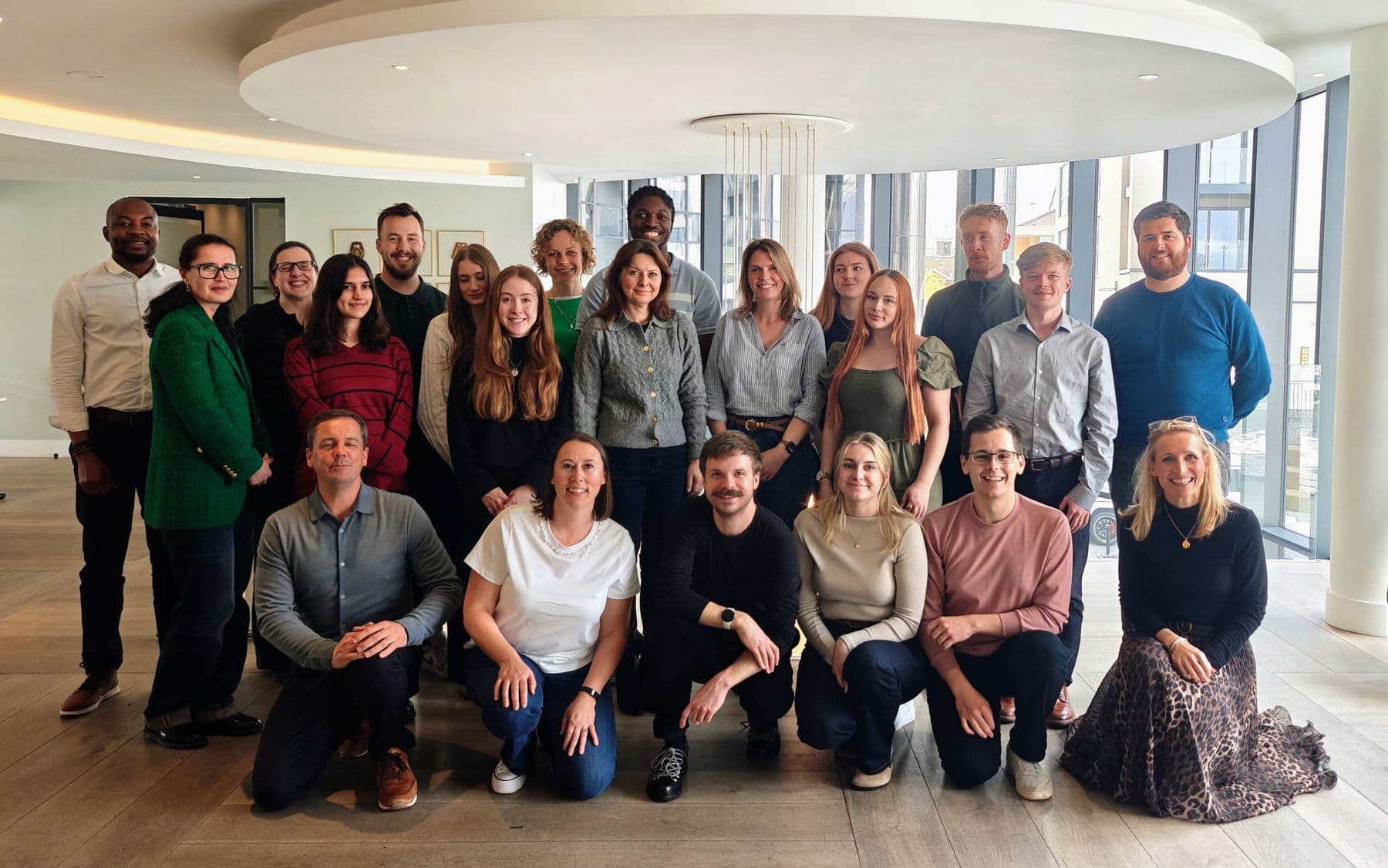 A large team gathered together for a photograph in a bright meeting room after a team day