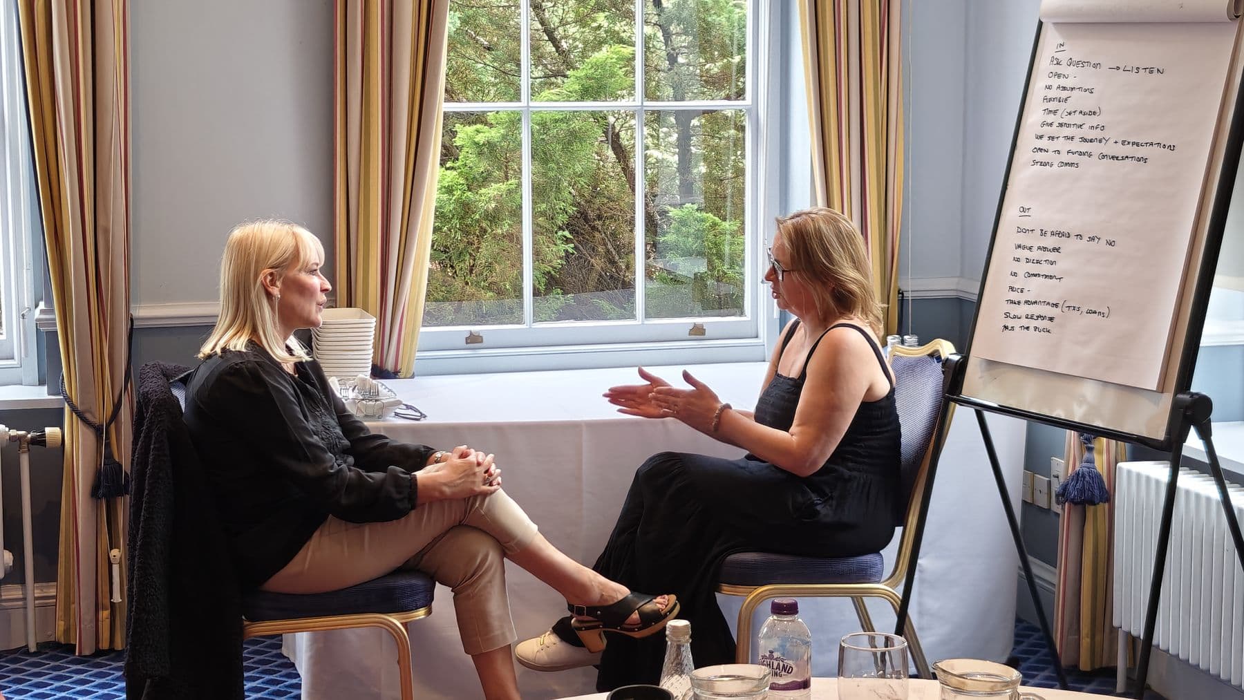 Two women sitting facing each other in a coaching practice session by a window