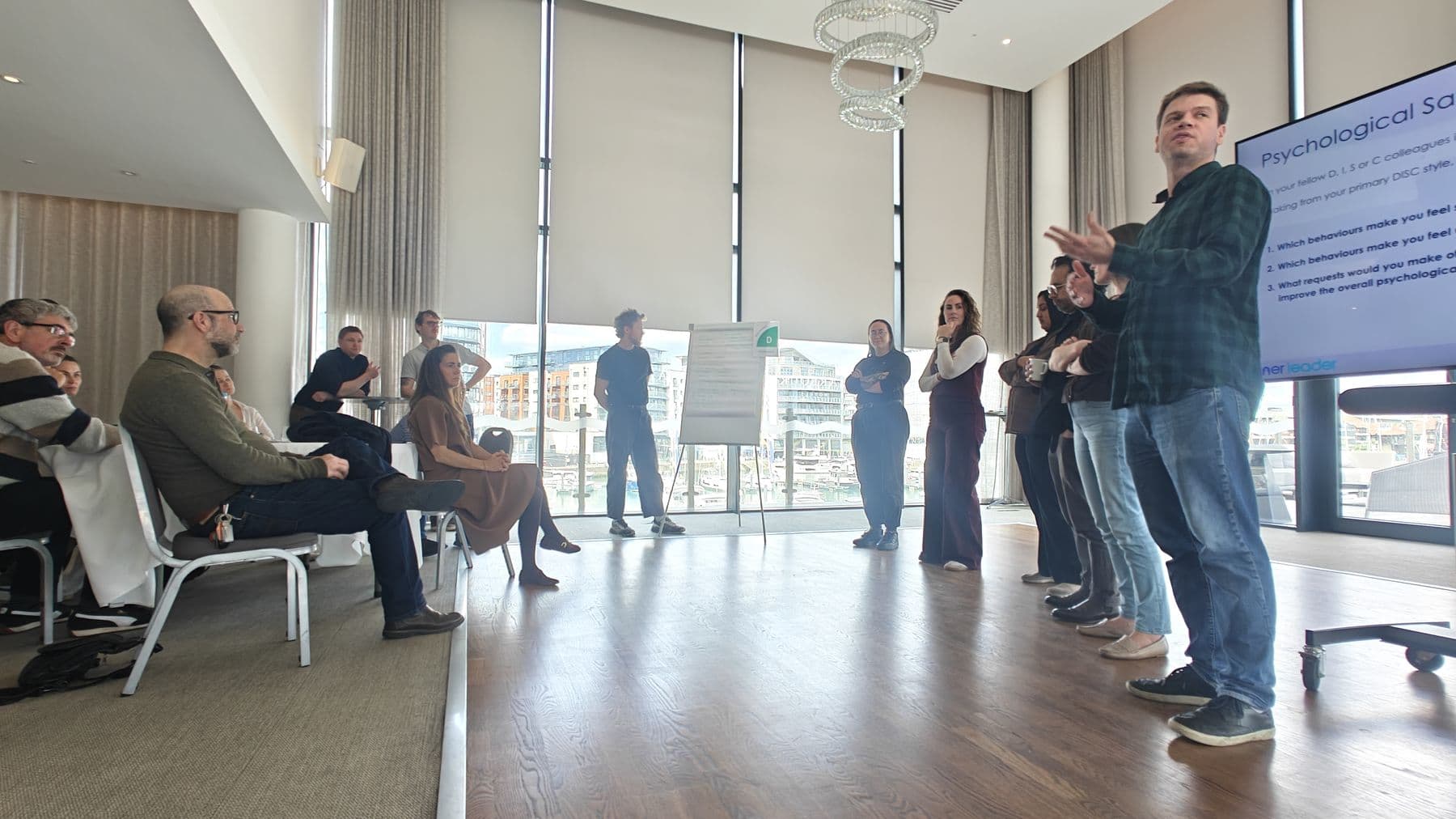 Participants standing in a line across a bright room during an exercise, while the facilitator talks