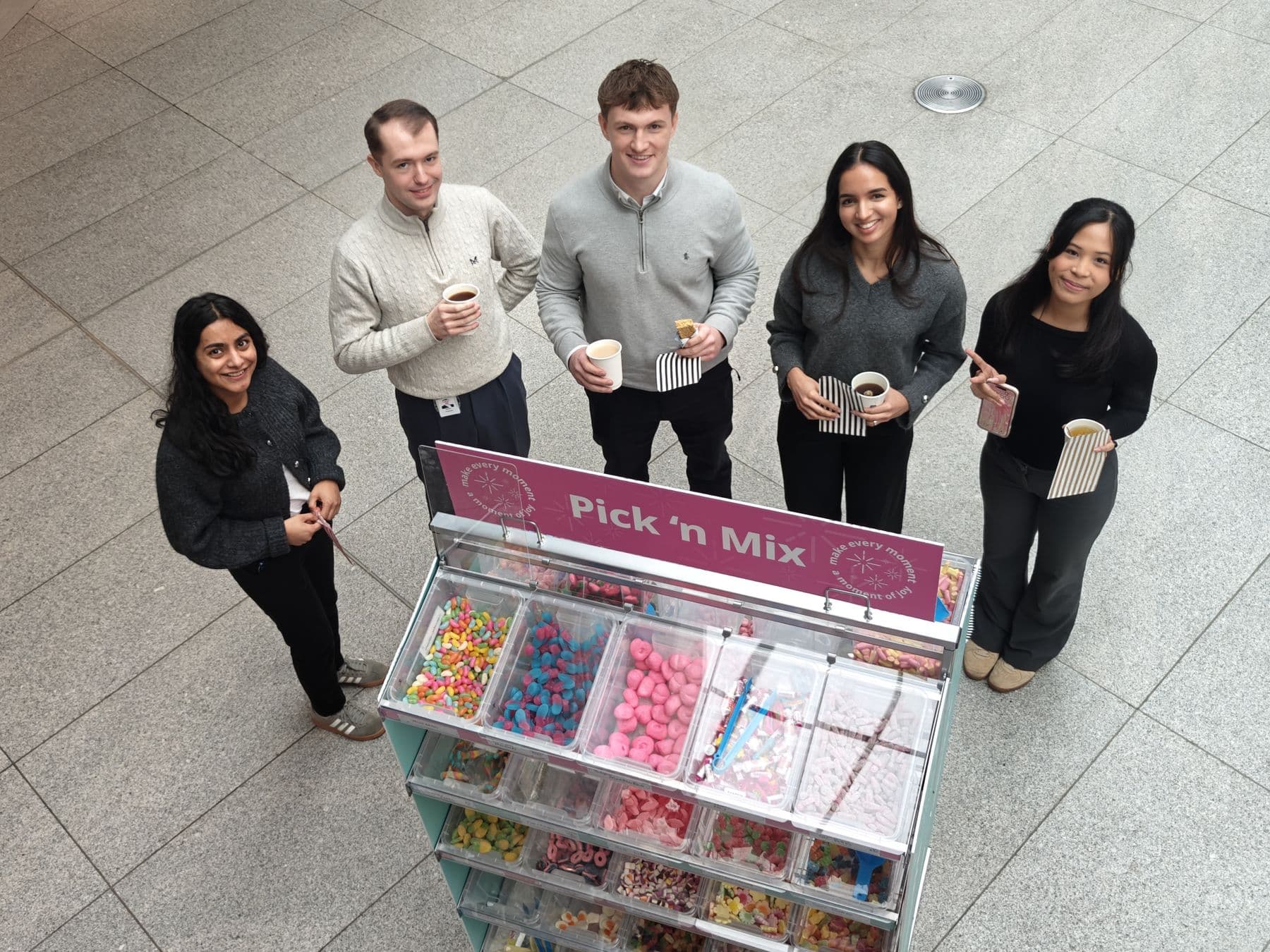 Graduates smiling up at the camera beside a pick and mix stand during a training day