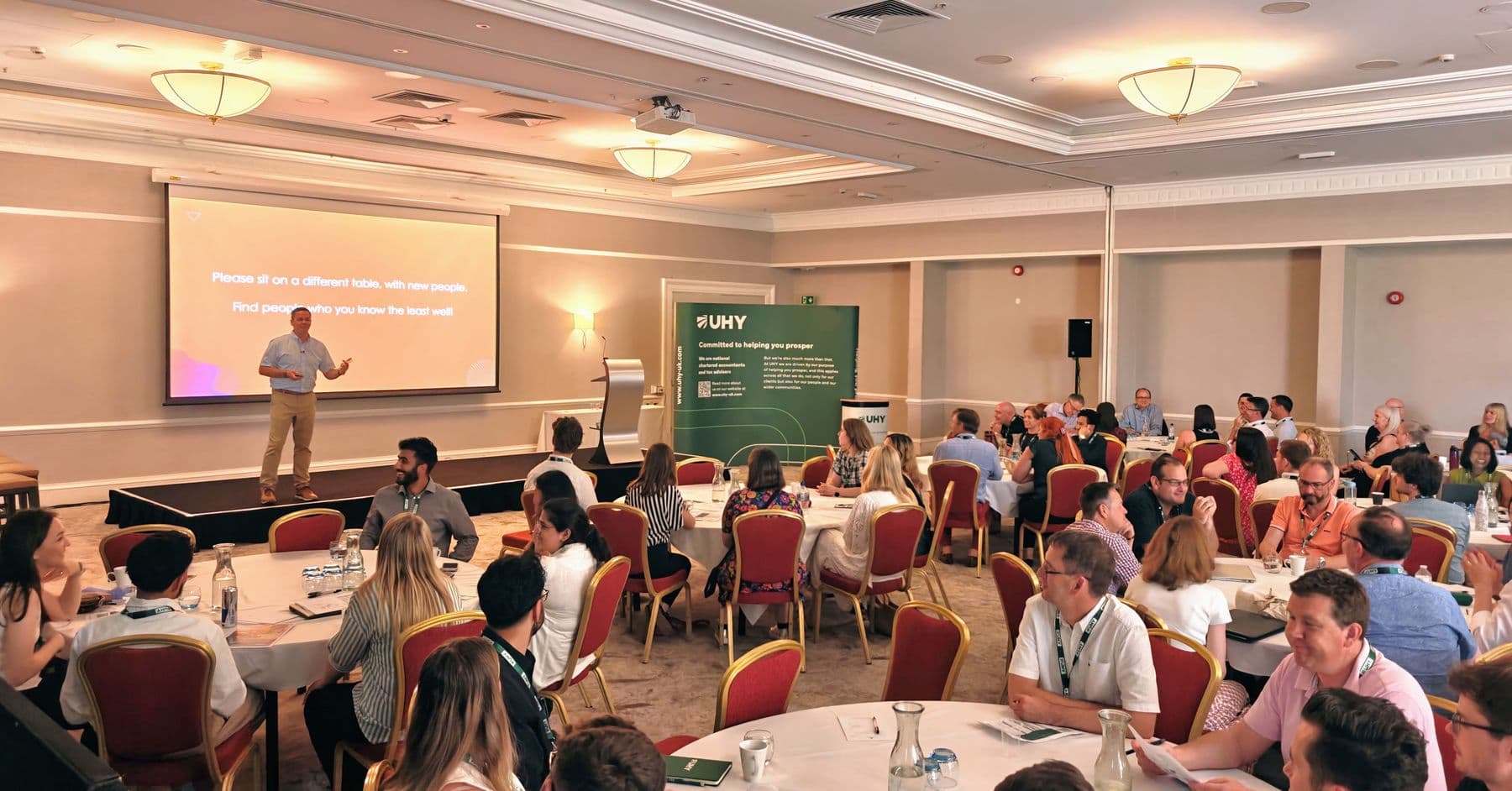 A conference room full of round tables as a speaker presents from the stage