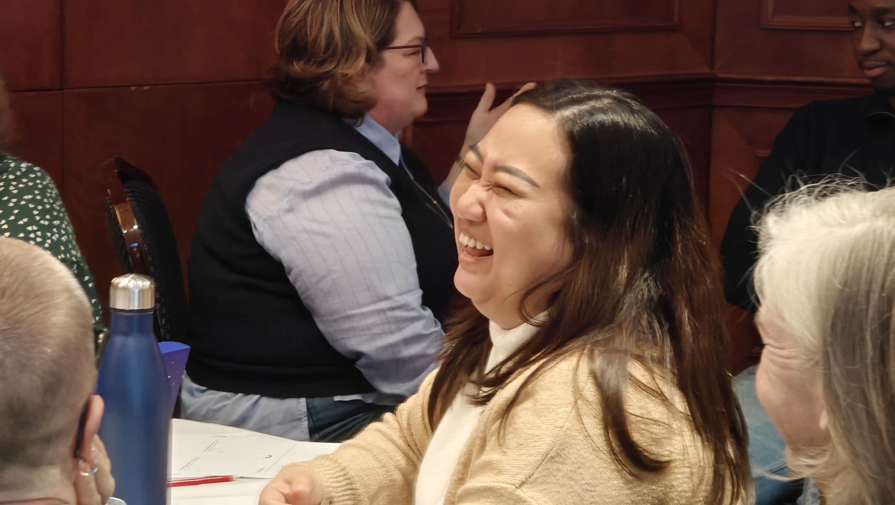 A participant laughing with colleagues at a workshop table