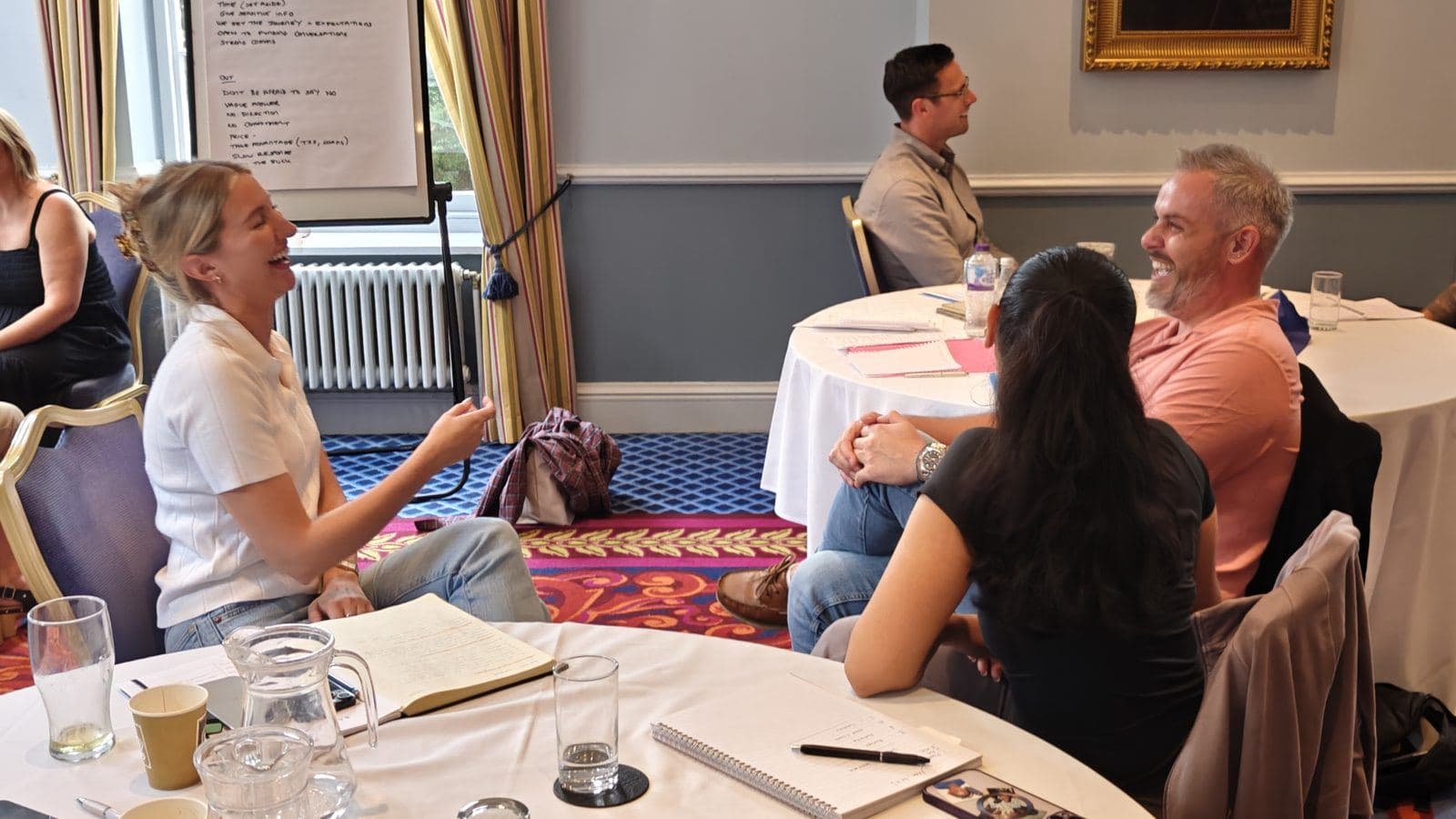 A workshop group at round tables, one participant making a point while the others listen